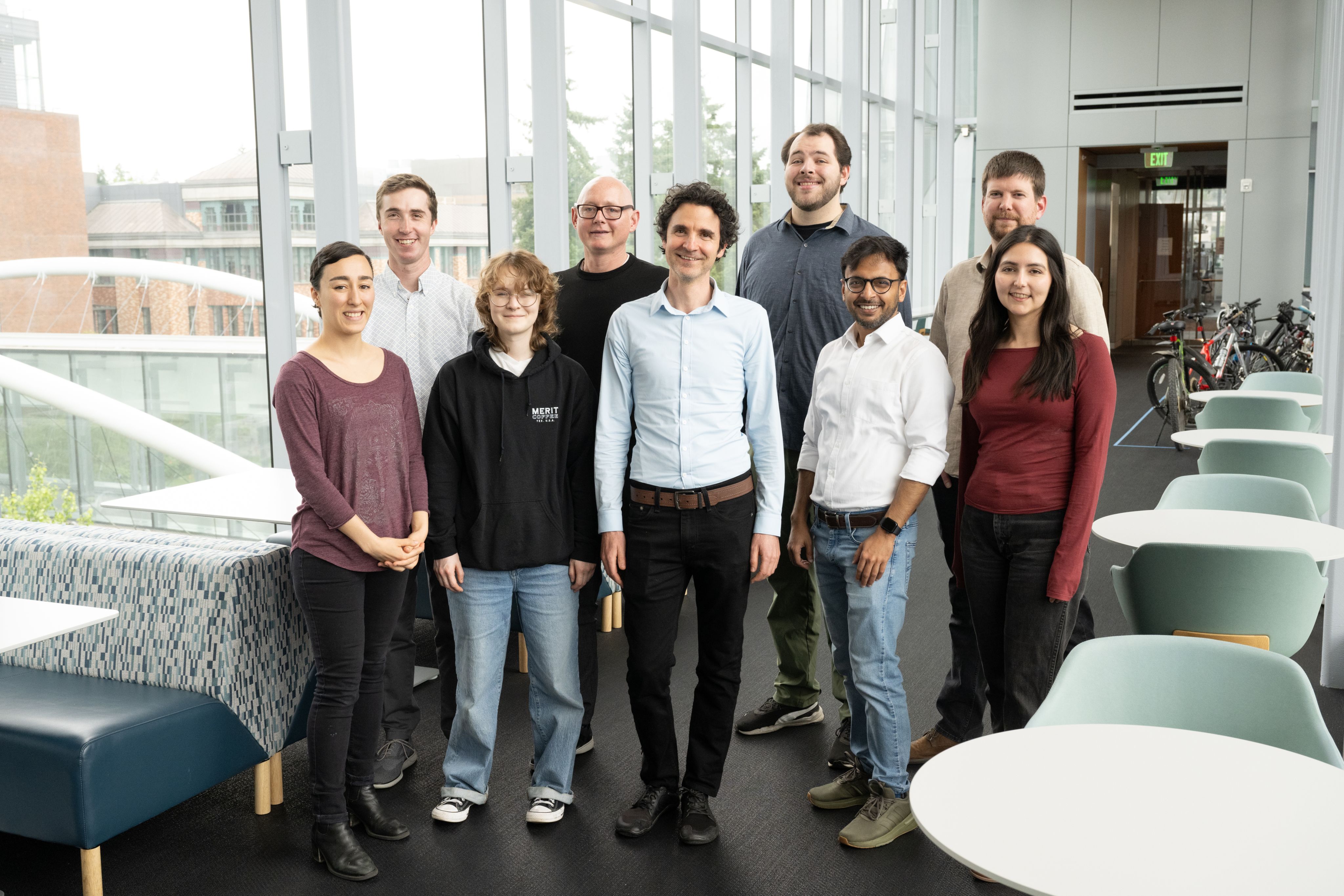 A group of scientist, wearing casual clothes, posing for a group shot in a glass building.