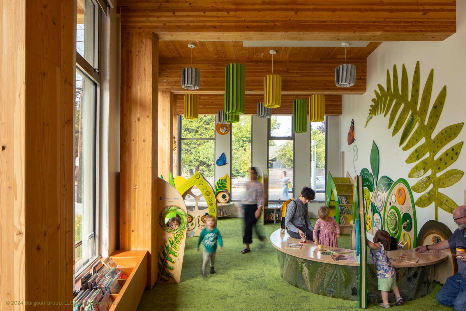 Inside the Holgate Library children's area. The space has lots of windows, wood beams and giant plant leaves pained on the wall. 