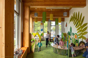Inside the Holgate Library children's area. The space has lots of windows, wood beams and giant plant leaves pained on the wall. 