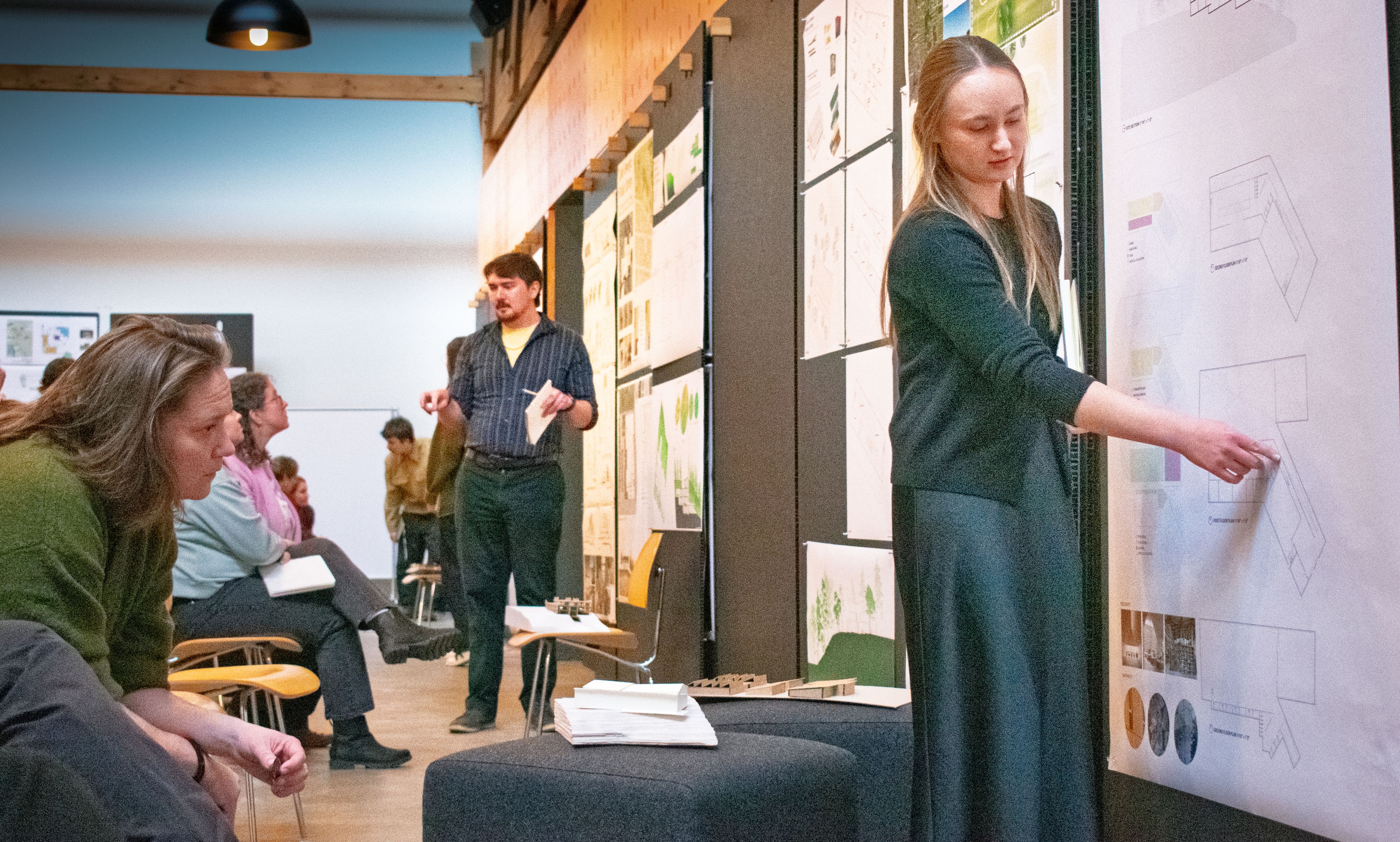 Students present their work during a midterm review at the Bora office. Posters line the wall and the audience listens intently. 