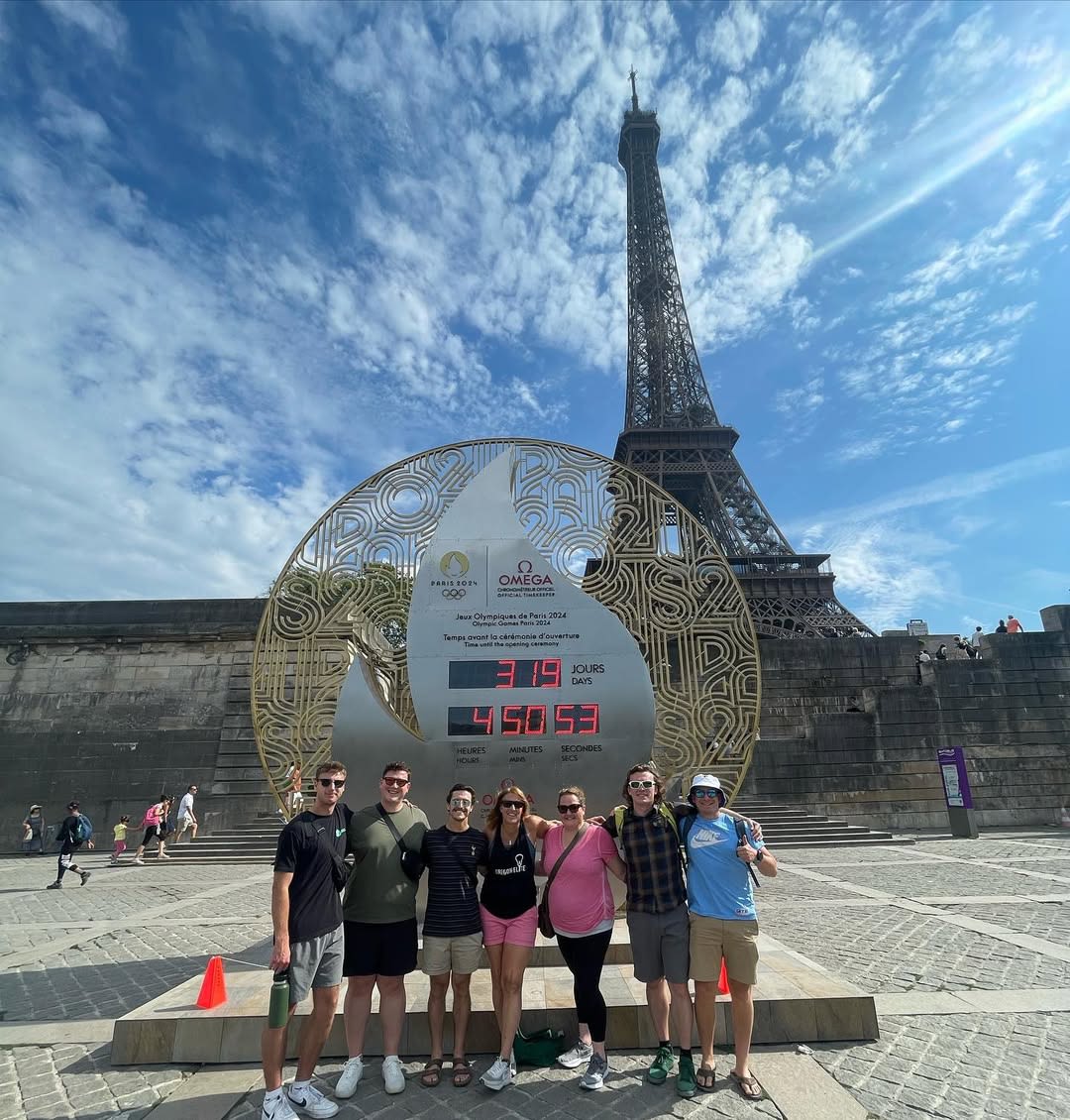 Oregon MBA students and faculty standing in front of an official Olympic clock while next to the Eiffel tour in Paris.