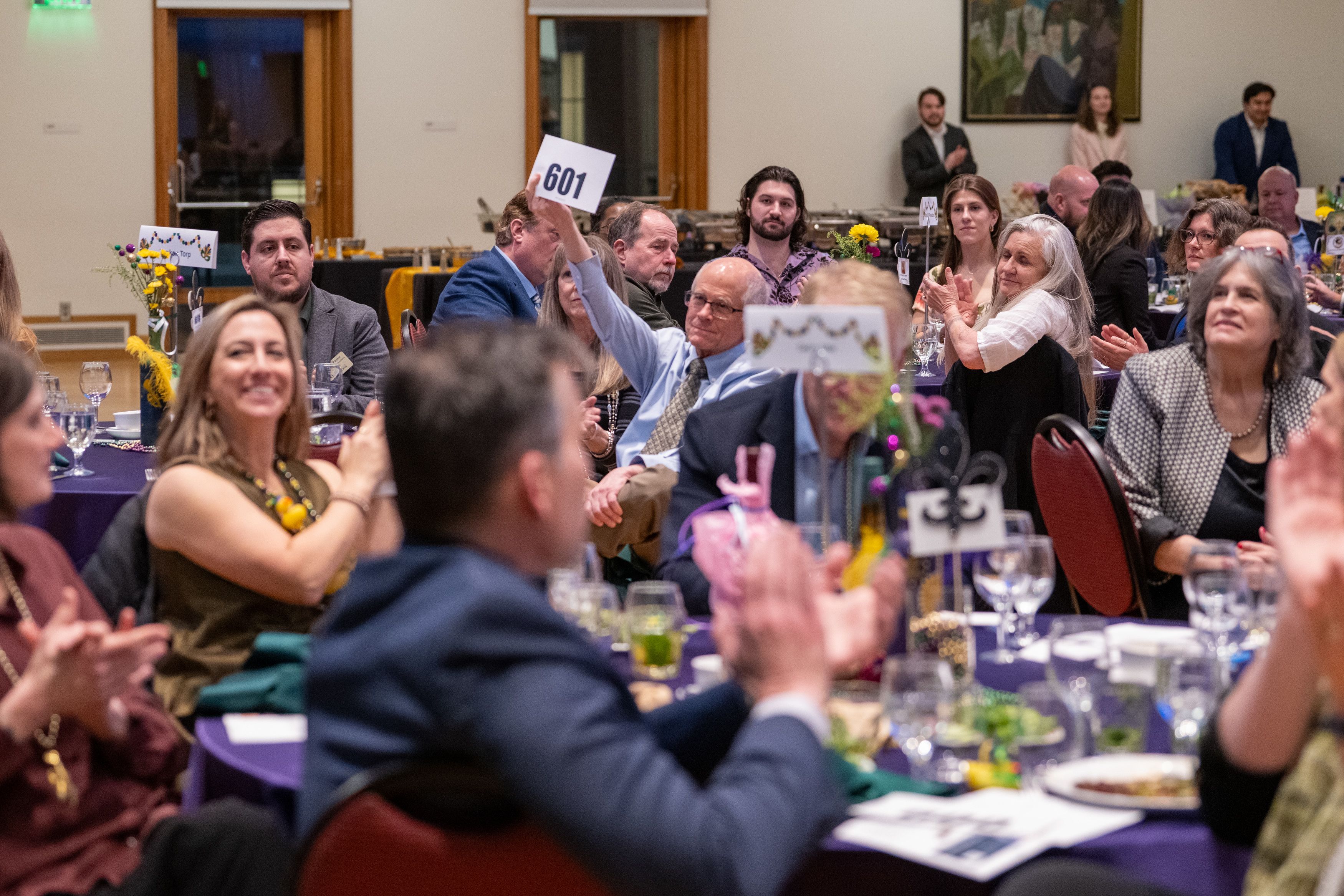 People clapping for guests raising paddle to give money. 