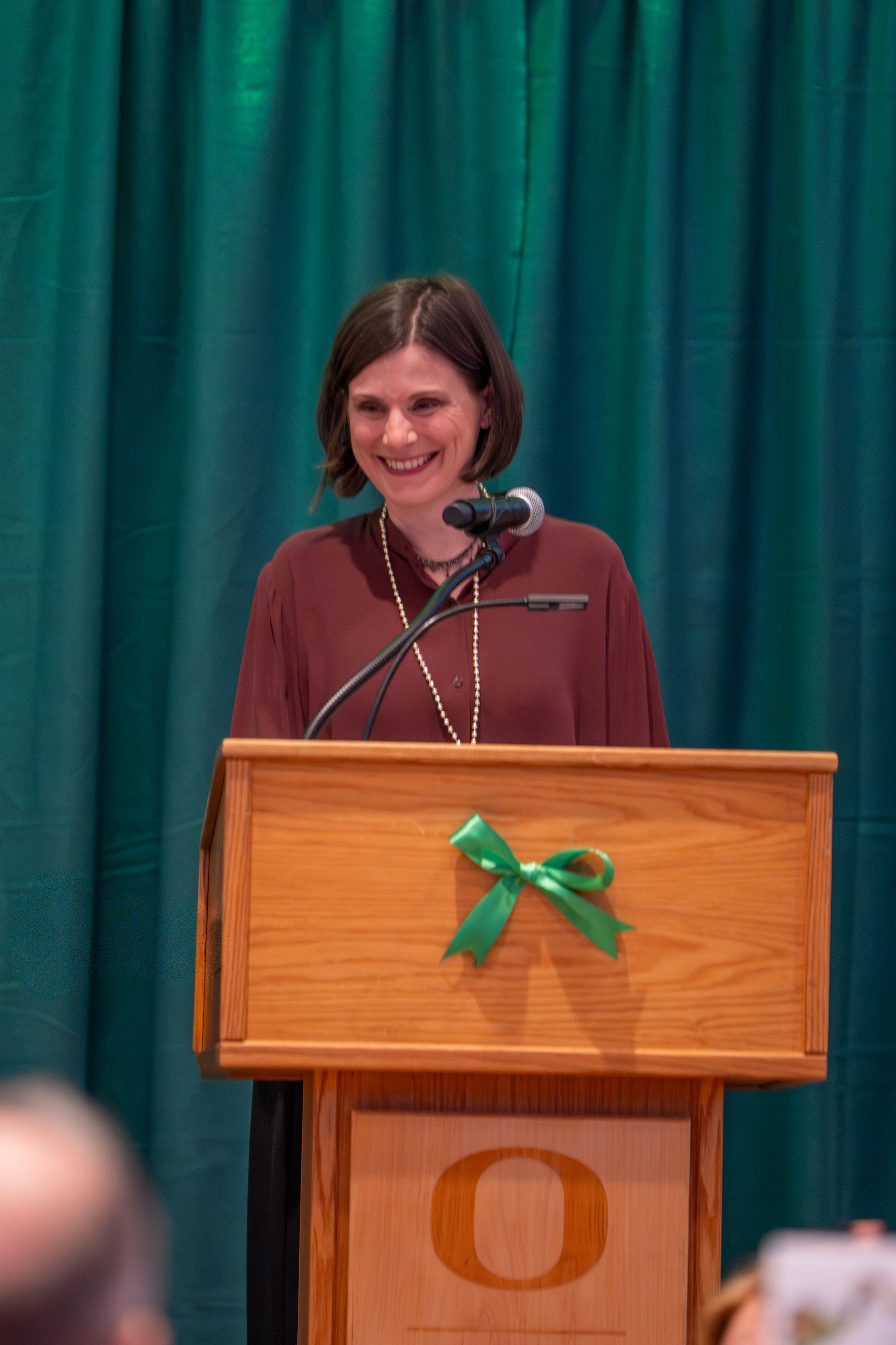 Dean Jen Reynolds smiling standing at a microphone.