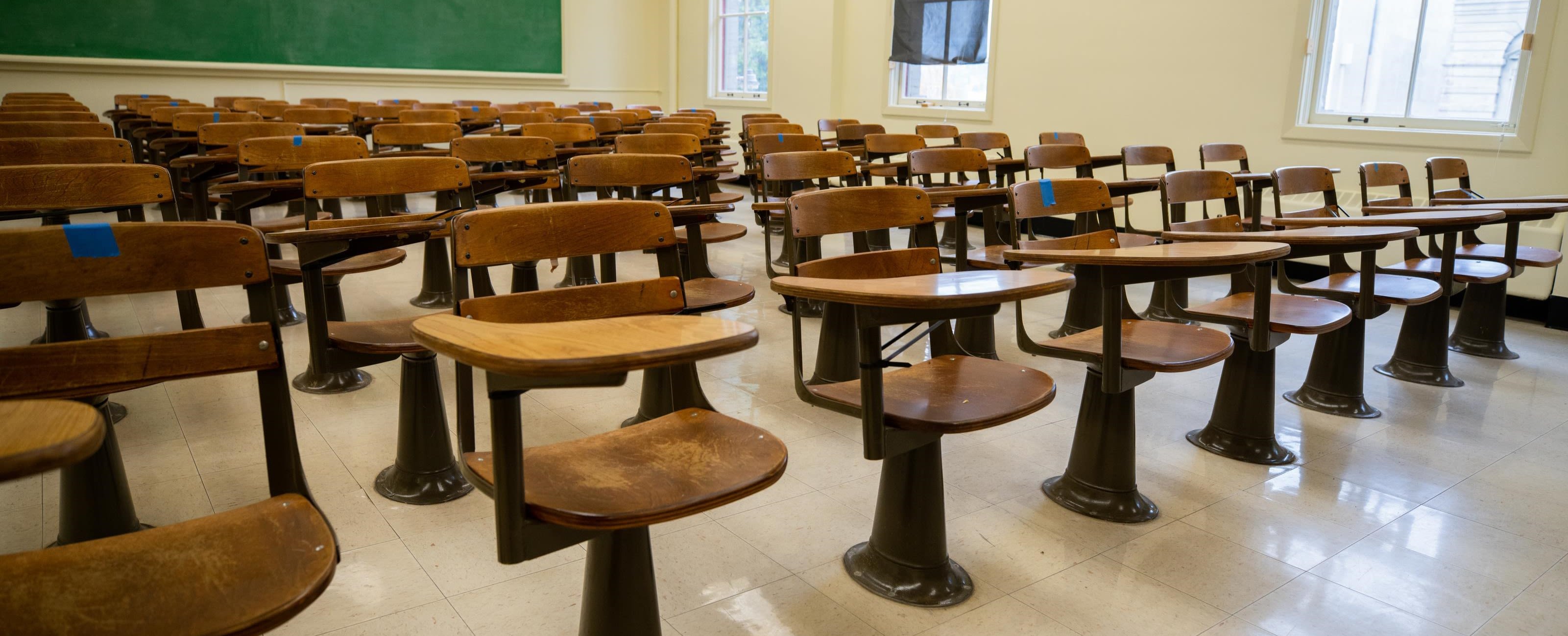 Rows of empty wooden desks in a classroom.